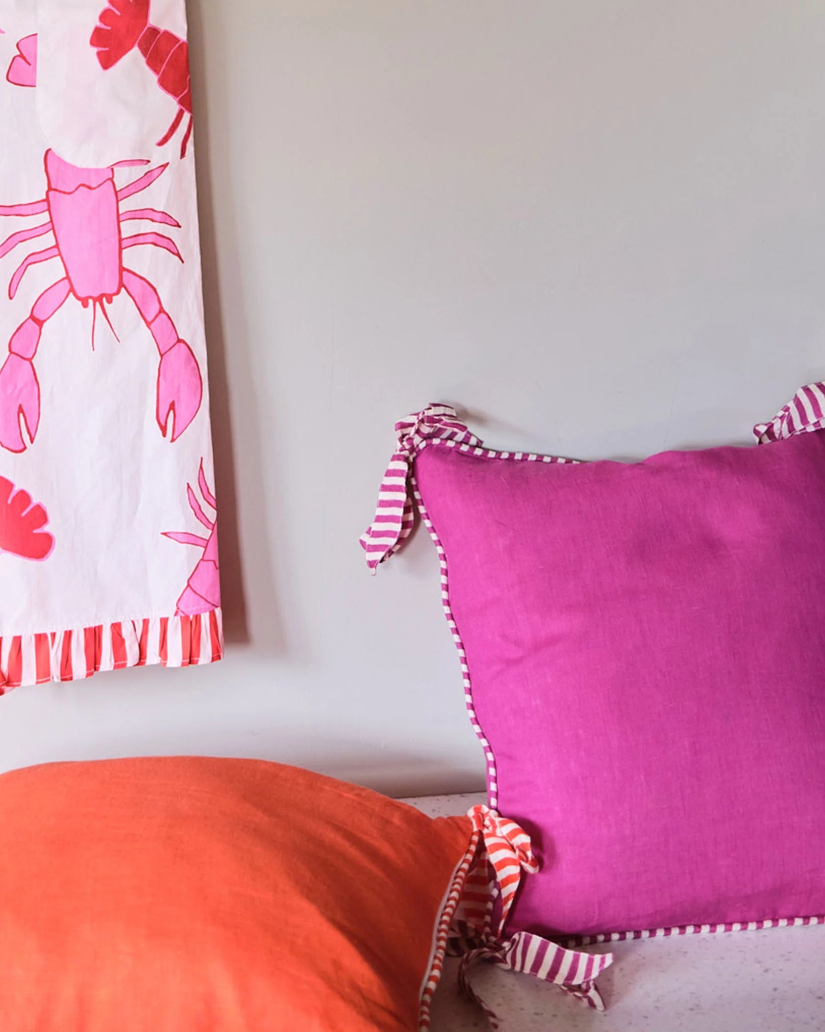 Two decorative Amuse la Bouche cushions one orange and one Fuchsia, both edged with striped piping and bows.
Feather inner included.