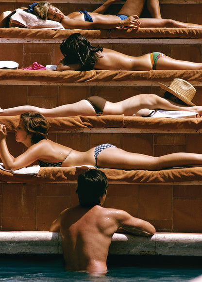 People sunbathing on brown towels by a poolside.